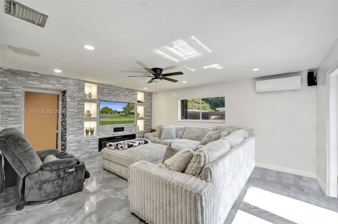 Stacked stone accent wall with integrated shelving, built-in electric fireplace, recessed lighting, ceiling fan, and tile flooring