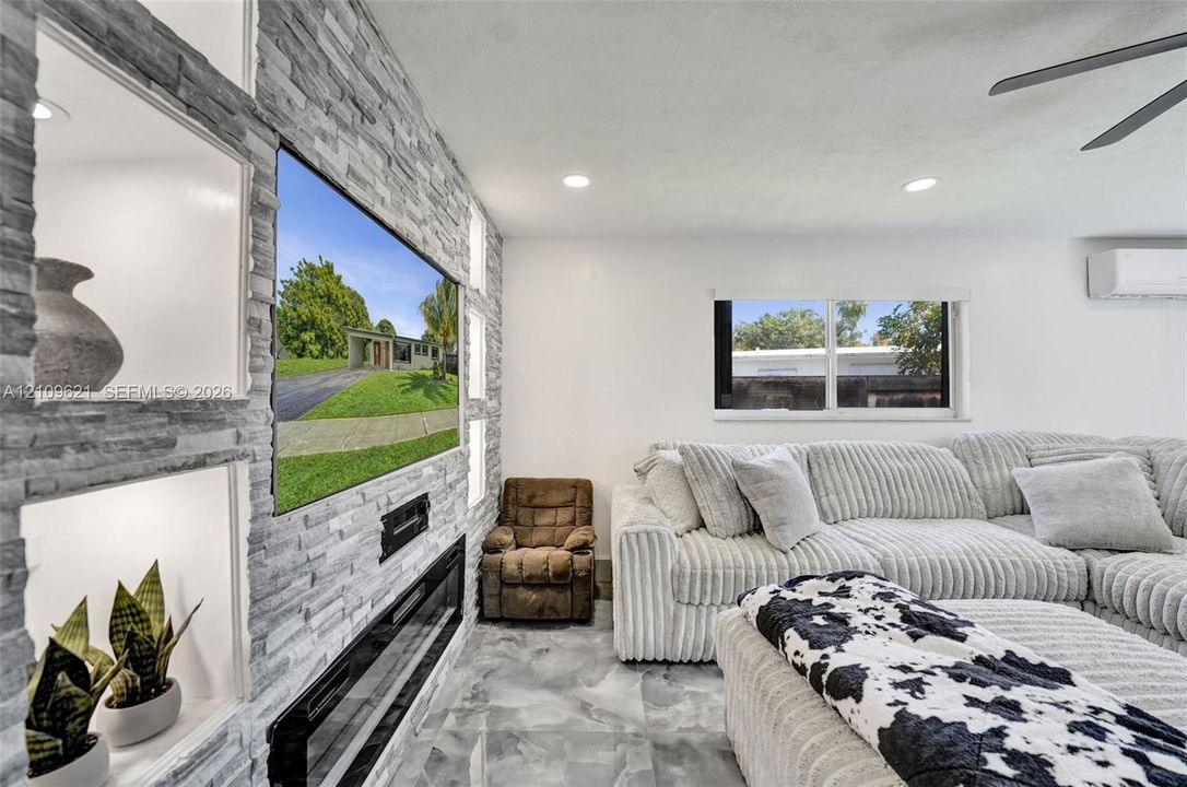 Stacked stone accent wall featuring built-in recessed shelving, a linear electric fireplace, recessed ceiling lighting, and polished stone-finish flooring