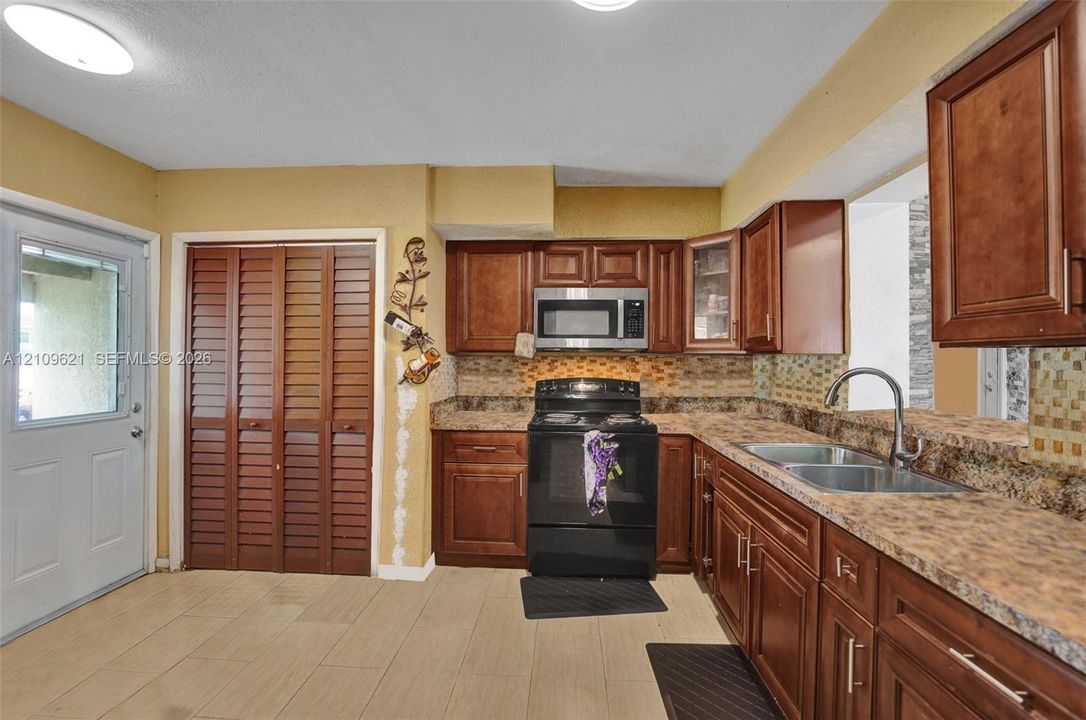 Kitchen featuring wood cabinetry, stone-pattern laminate countertops, tiled backsplash, stainless steel microwave, and dual-basin stainless steel sink