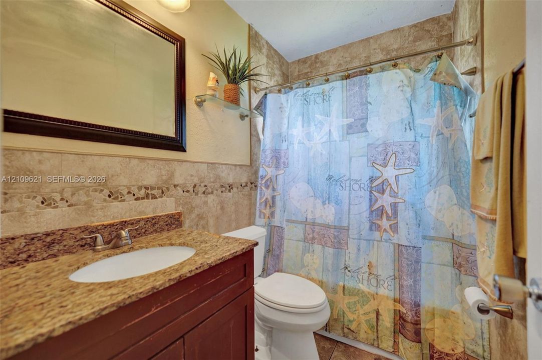 Bathroom featuring a stone-finish countertop with an integrated oval basin, dark wood-finish vanity cabinetry, full-wall tiling with decorative inlay, and a wall-mounted mirror