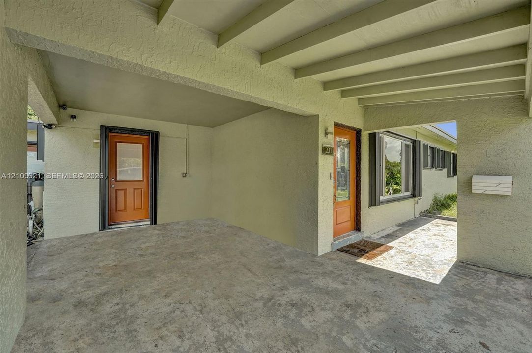 Covered carport with exposed beam ceiling, stucco exterior walls, two solid-core doors with glass inserts, and concrete flooring