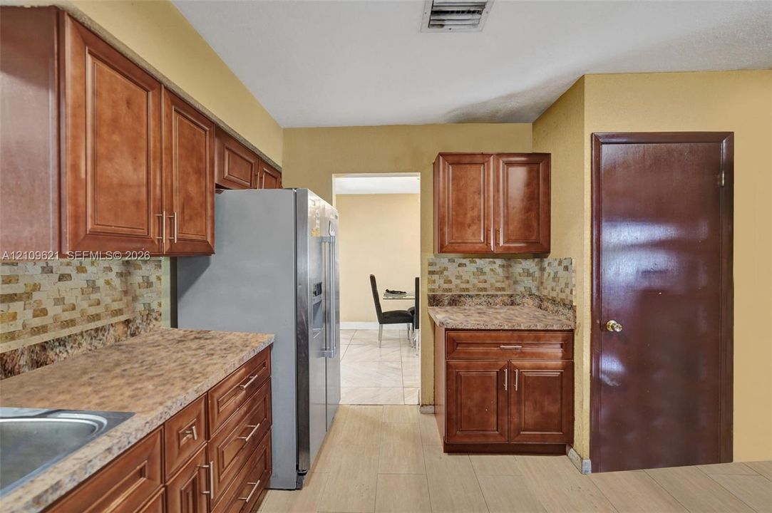 Kitchen featuring wood-finish cabinetry, stone-patterned laminate countertops, and a textured tile backsplash