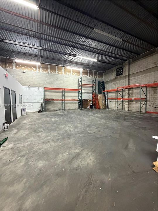Open-concept industrial warehouse space featuring high ceilings with exposed steel trusses, polished concrete flooring, concrete block walls, and integrated metal racking systems