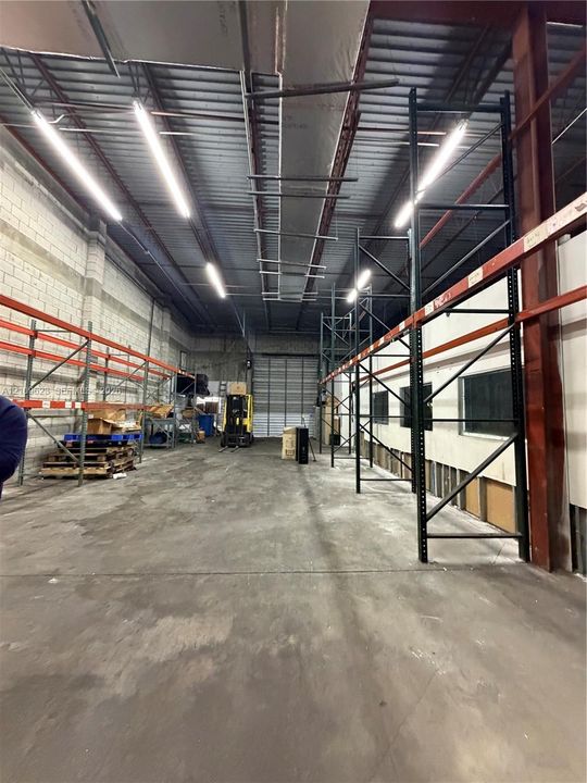 Industrial warehouse space featuring high ceilings, exposed structural steel, heavy-duty industrial racking, concrete flooring, and linear overhead lighting