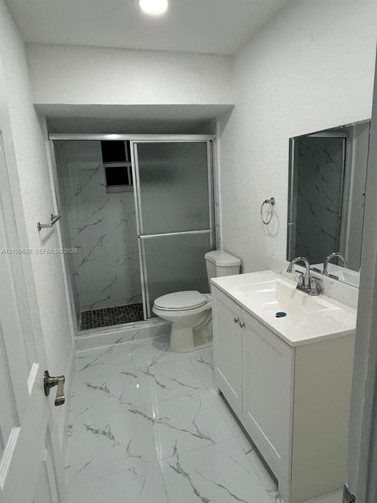 Bathroom featuring white cabinetry with integrated countertop, polished large-format tile flooring, shower enclosure with glass doors, and decorative wall tiling