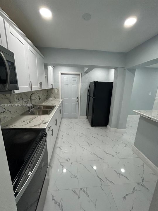 Kitchen featuring white shaker-style cabinetry, stone-patterned countertops, large-format tiled flooring, recessed lighting, and integrated stainless steel microwave