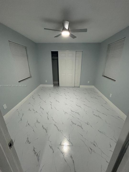 Interior space featuring light-toned, high-contrast patterned flooring, dual windows with integrated blinds, a ceiling fan with integrated lighting, and a closet with sliding paneled doors