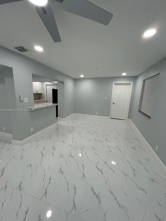 Polished tile flooring with high-contrast veining, recessed lighting, ceiling fan, and a pass-through breakfast bar featuring stone-surface countertop