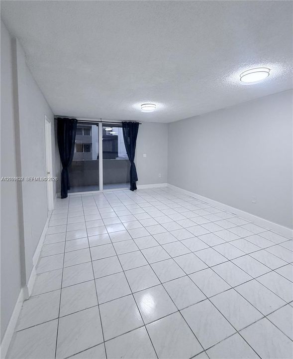 Neutral-toned interior space featuring light-colored square tile flooring and sliding glass doors with external access
