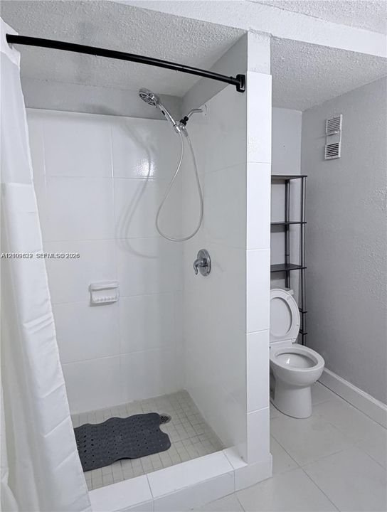Bathroom featuring a shower stall with white tile surround, a handheld shower fixture, and a standard toilet