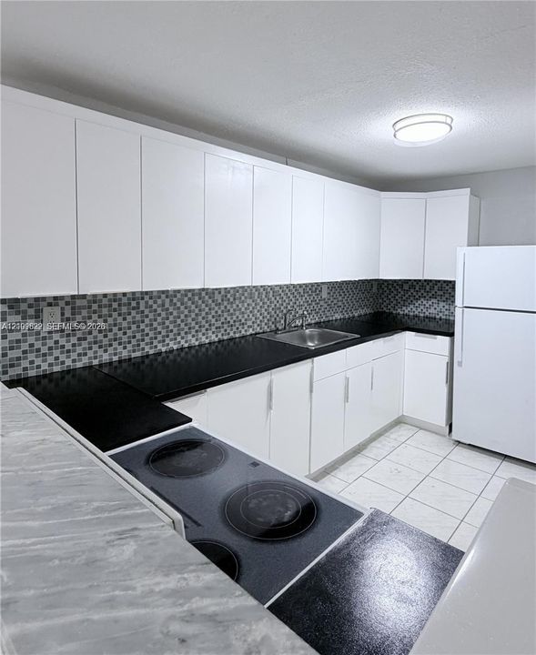 Kitchen featuring white cabinetry, black countertops, mosaic tile backsplash, built-in cooktop, and tile flooring