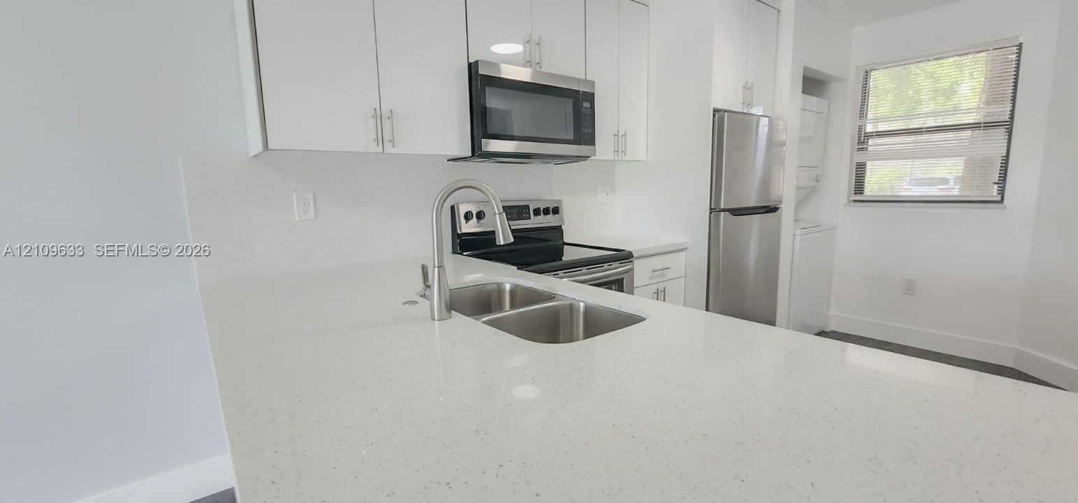Kitchen featuring white cabinetry, quartz countertops, stainless steel appliances, a double-basin undermount sink with a gooseneck faucet, and a stacked laundry unit