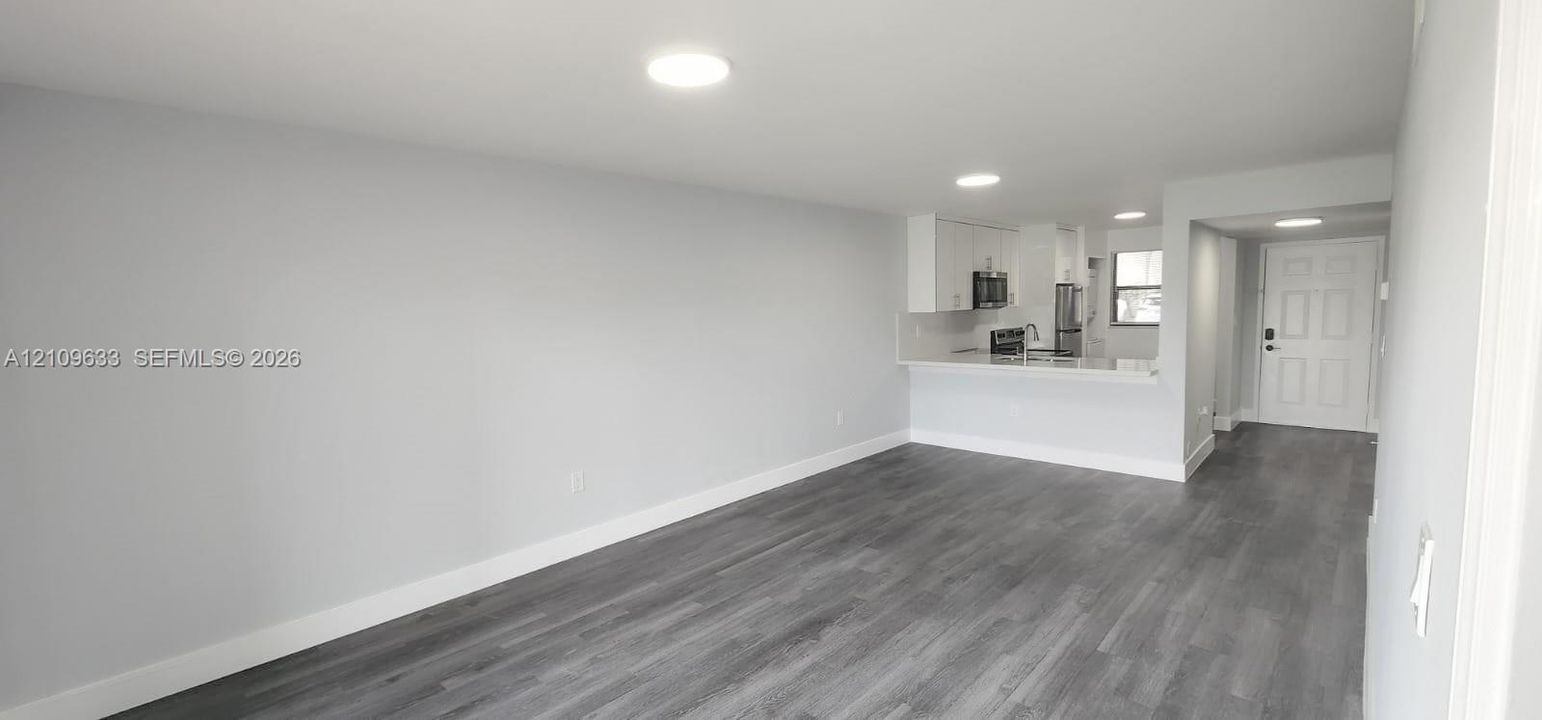 Open-concept interior featuring wood-finish flooring, recessed lighting, and a kitchen equipped with white cabinetry and a breakfast bar