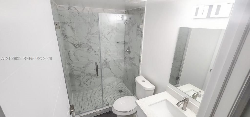 Bathroom featuring a glass-enclosed shower with floor-to-ceiling stone-finish tile, a vanity with a rectangular basin, an integrated mirror, and wall-mounted lighting