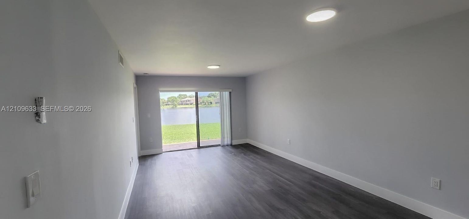 Interior space featuring dark wood-finish flooring, neutral wall paint, recessed ceiling lighting, and sliding glass doors with outdoor water access