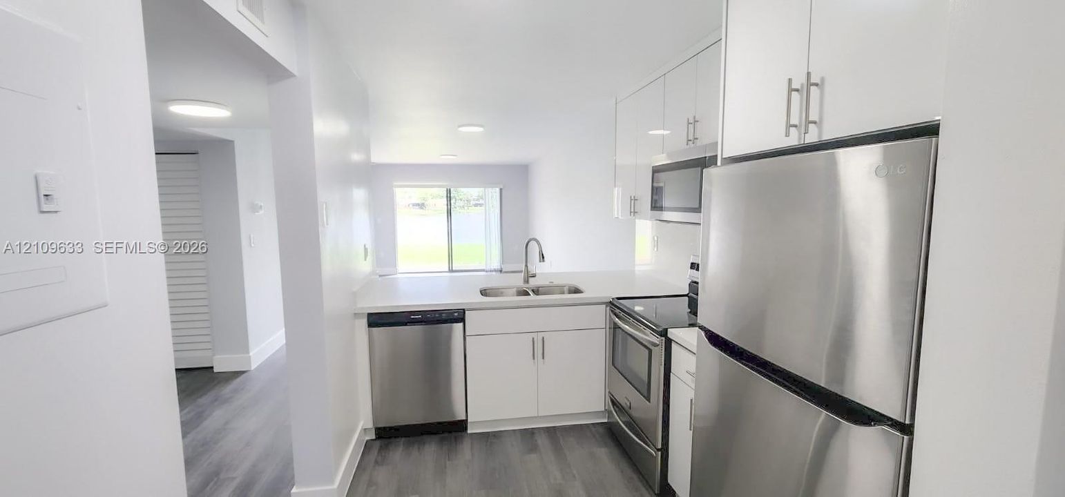 Kitchen featuring high-gloss white cabinetry, stainless steel appliances, solid-surface countertops, dual-basin sink, and wood-finish flooring