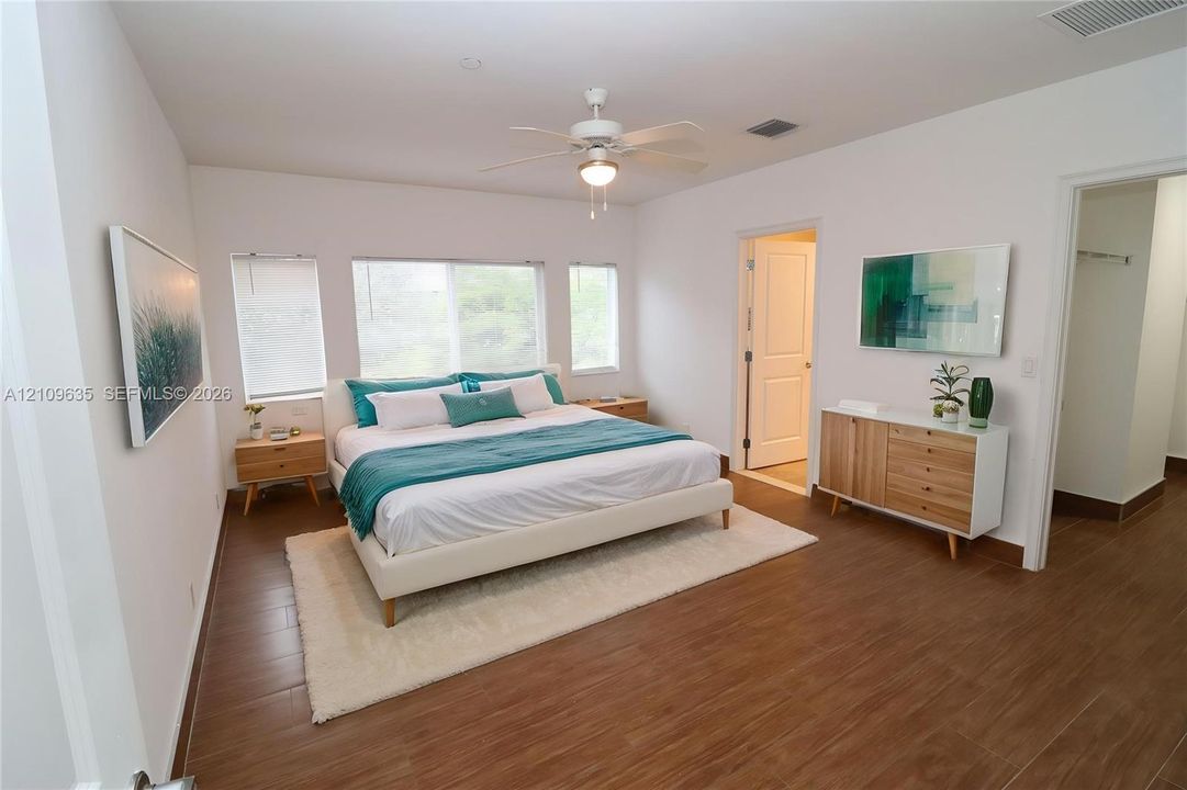 Bedroom featuring wood-finish tile flooring, three paneled windows, and a central ceiling fan with integrated lighting