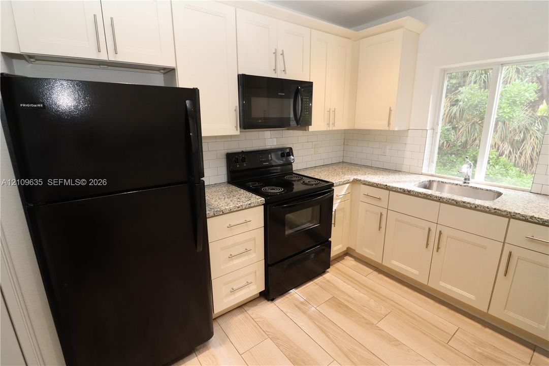 Kitchen featuring off-white shaker-style cabinetry, speckled stone countertops, a white subway tile backsplash, wood-finish tile flooring, and integrated black appliances