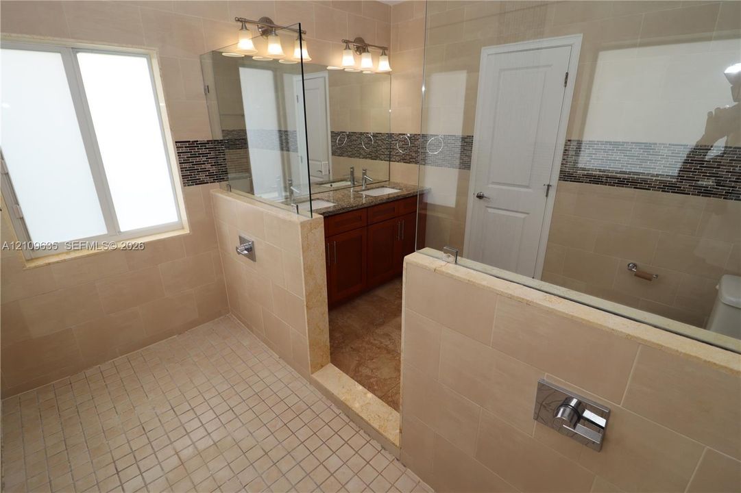 Bathroom featuring a dual-sink vanity with stone countertop, frameless glass shower enclosure, large-format tile surround with glass mosaic inlay, and tile flooring