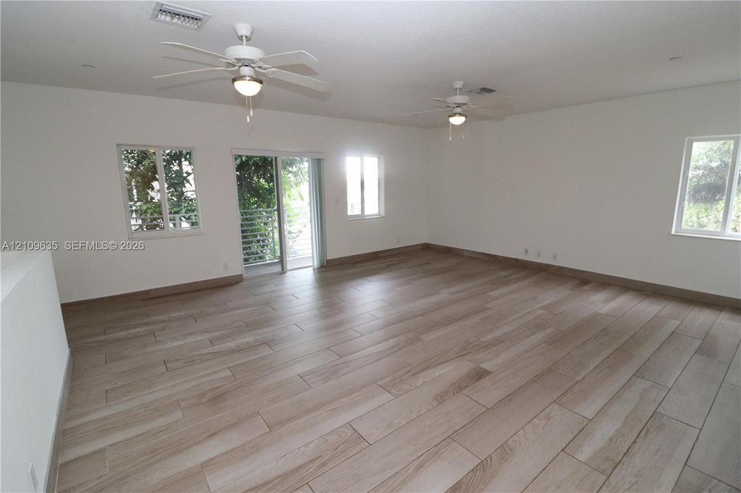 Spacious interior featuring wood-finish tile flooring, dual ceiling fans, multiple windows, and a glass sliding door
