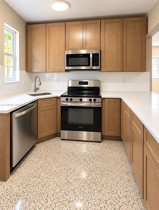 Kitchen featuring shaker-style cabinetry, white quartz countertops, stainless steel appliances, and terrazzo flooring