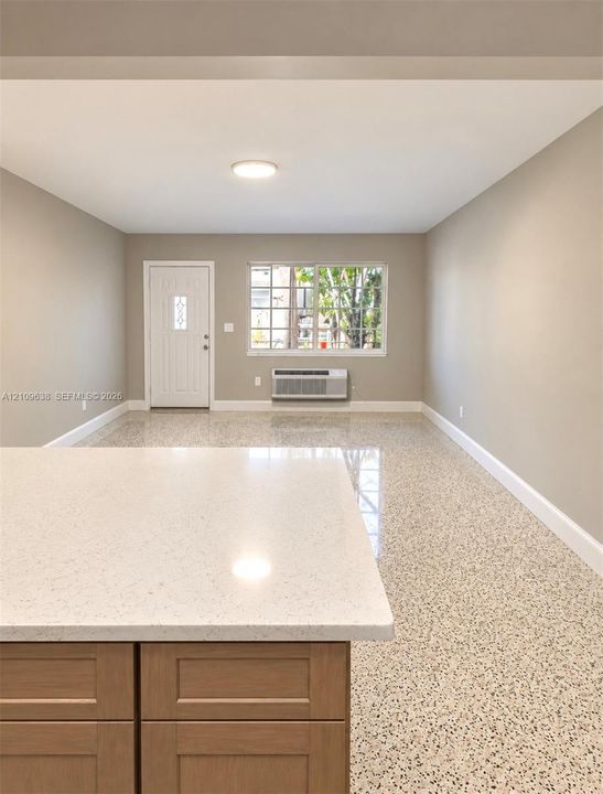 Polished terrazzo flooring, neutral wall tones, white quartz countertop, Shaker-style wood-finish cabinetry, and a grid-pane window