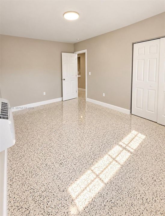 Neutral-toned interior room featuring polished terrazzo flooring, flush-mount ceiling lighting, a white six-panel interior door, and a white bi-fold closet door