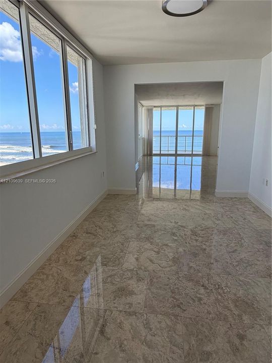 Polished stone flooring, expansive floor-to-ceiling windows, and sliding glass doors leading to a balcony, featuring direct ocean exposure