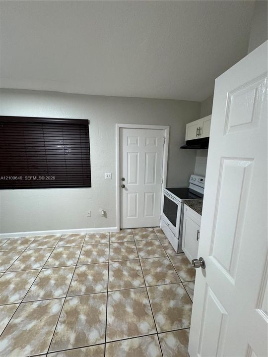 Kitchen area featuring patterned ceramic tile flooring, white cabinetry, a stone-finish countertop, a white freestanding range, and a window with dark horizontal blinds