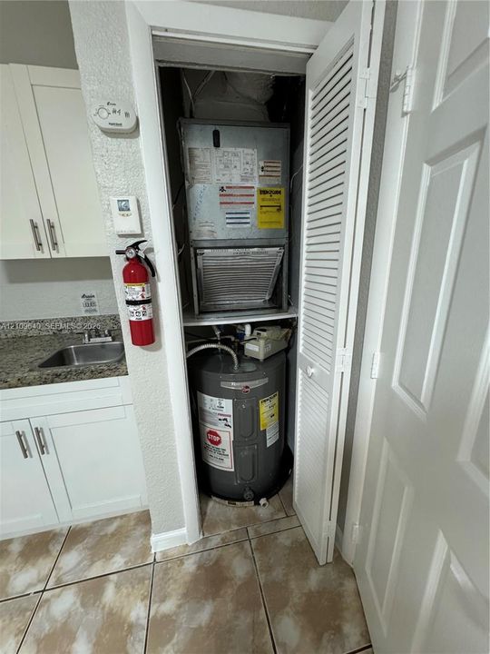 Utility closet housing an HVAC air handler and water heater, featuring white louvered doors