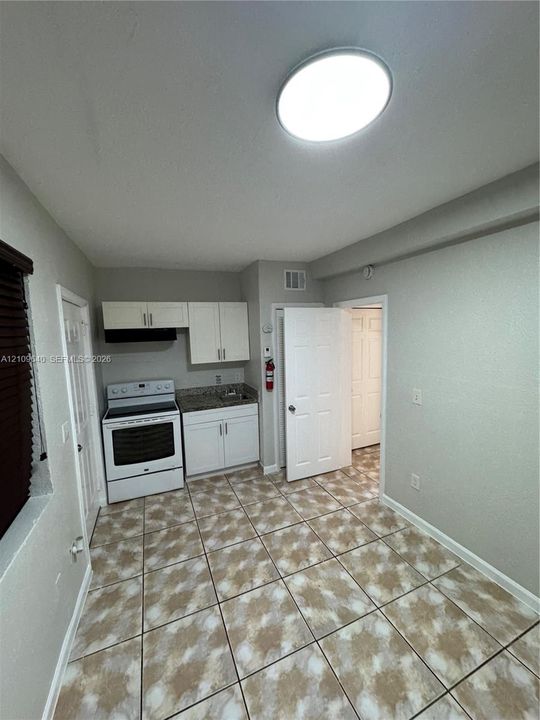 Kitchenette featuring white cabinetry, stone-finish countertops, a built-in range, and tile flooring