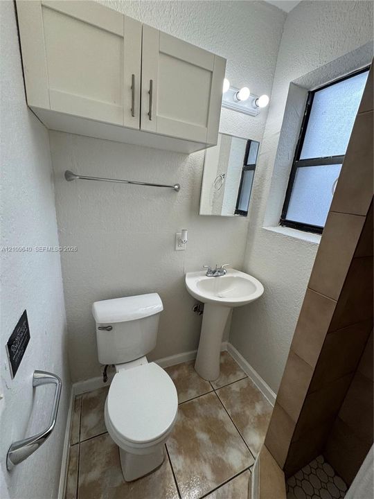 Bathroom featuring a pedestal sink, white cabinetry, tiled flooring, wall-mounted lighting fixture, and a window