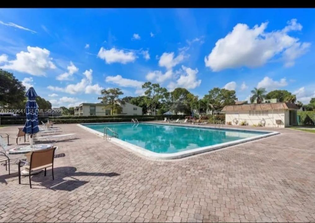 Rectangular swimming pool featuring a brick paver deck, metal safety handrails, and a nearby utility structure
