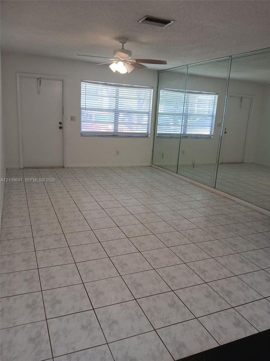Room interior featuring large-format tile flooring, wall-to-wall mirrored panels, a ceiling fan with integrated lighting, and a single-pane window