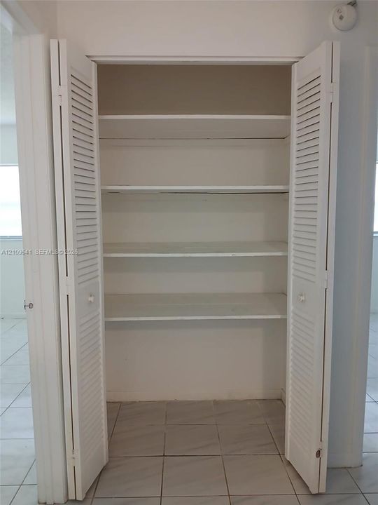Storage closet featuring dual white louvered doors and three built-in shelves