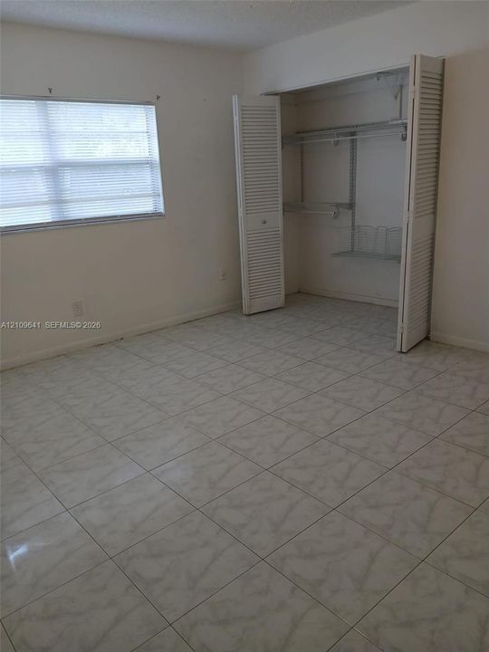 Room featuring neutral tile flooring, window with built-in blinds, and a closet with bifold louvered doors and integrated wire shelving