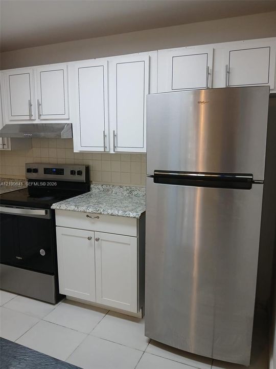 Kitchen featuring white shaker-style cabinetry, stone-finish countertops, stainless steel appliances, and a square-tile backsplash