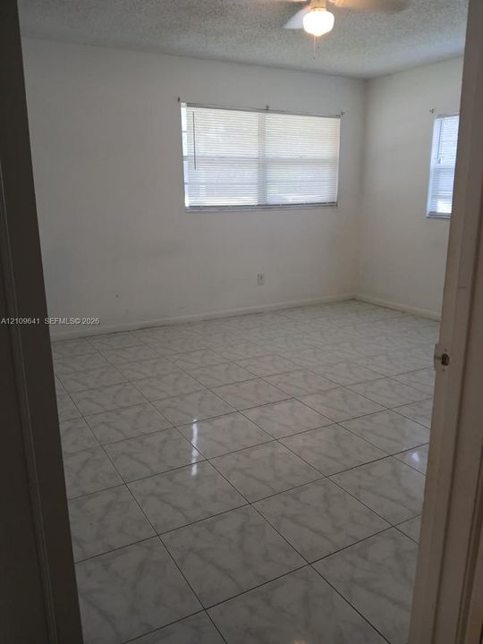 Interior room featuring neutral wall-to-wall ceramic tile flooring, dual windows, and an attached ceiling fan with light fixture