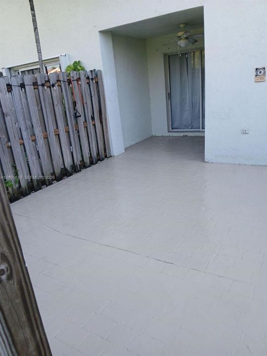 Covered concrete patio featuring a ceiling fan and vertical wood privacy fencing