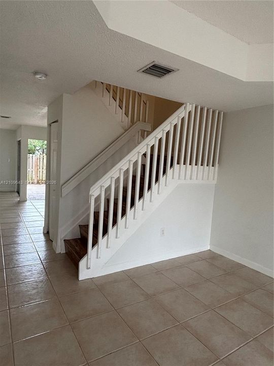 Staircase featuring white balusters, a wooden handrail, and wood-finish treads, complemented by neutral tile flooring throughout the open floor area