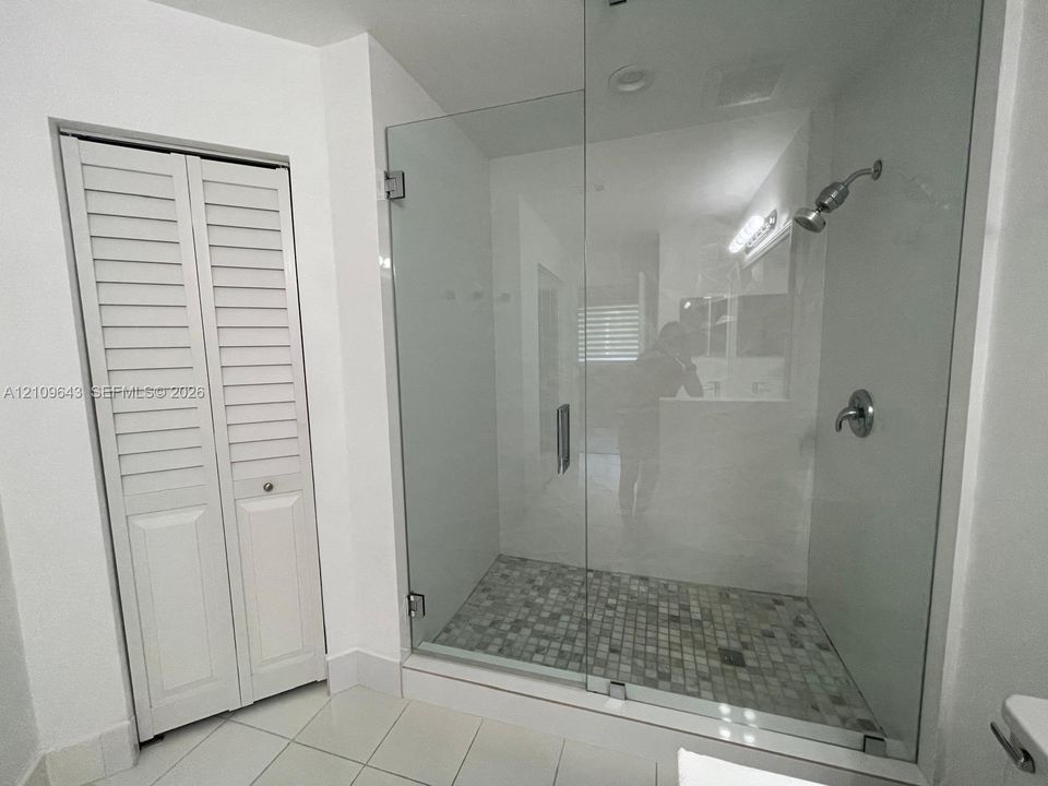 Walk-in shower featuring a frameless glass enclosure, pebble-tile flooring, and metallic fixtures