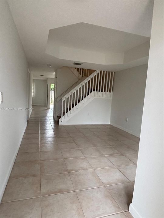 Interior space featuring large-format ceramic tile flooring, a tray ceiling, and a wooden staircase with white balusters