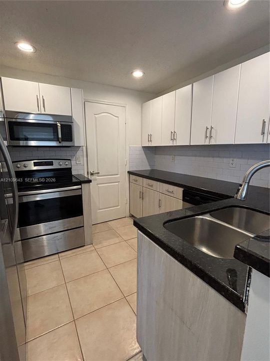 Kitchen featuring stainless steel appliances, dark stone-finish countertops, subway tile backsplash, recessed lighting, and white cabinetry