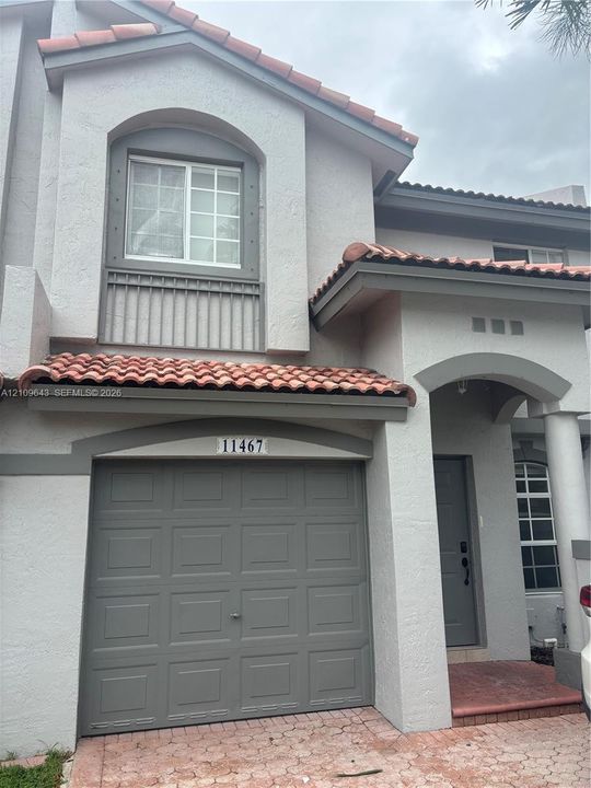 Stucco exterior featuring terracotta-style roof tiles, arched architectural detailing, a paneled garage door, and a covered entryway with column support