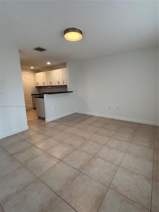 Ceramic tile flooring throughout the main space, featuring kitchen cabinetry with contrasting dark countertops, a stainless steel kitchen faucet, and a flush-mount circular ceiling fixture