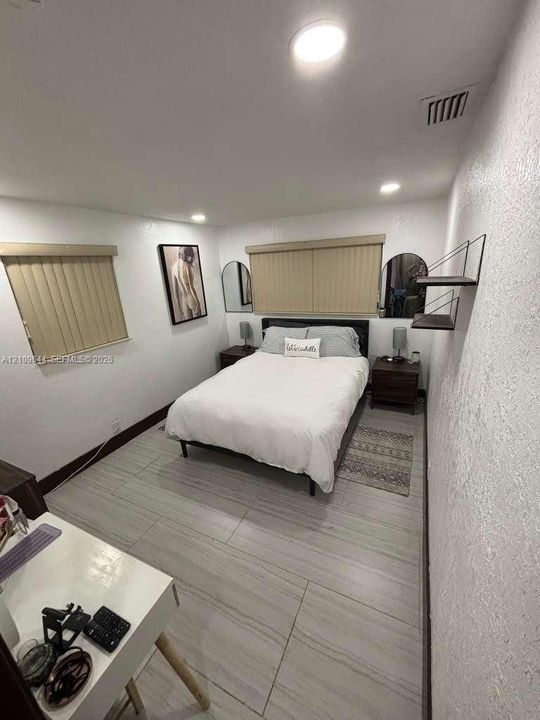 Large-format tile flooring, recessed ceiling lighting, and vertical window blinds