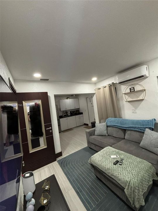 Living space featuring wood-finish flooring, recessed lighting, wall-mounted ductless air conditioning unit, and a dark-toned interior door with integrated mirror