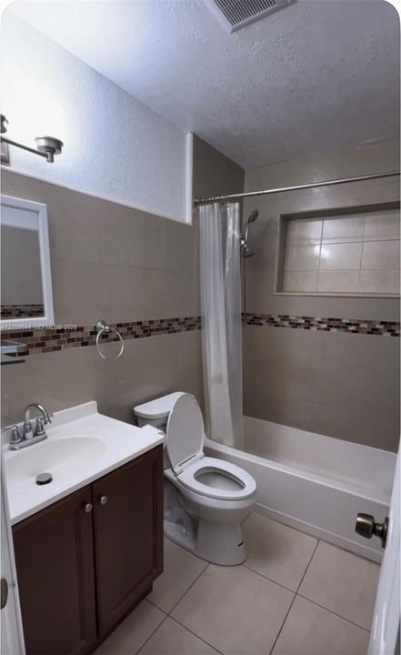 Bathroom featuring tile flooring, vanity with white countertop, integrated shower niche, and decorative mosaic tile backsplash