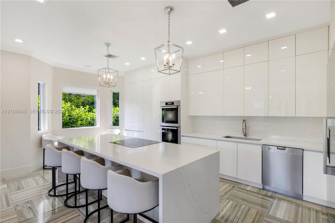 Modern kitchen featuring high-gloss cabinetry, stone-finish countertops, an oversized center island, built-in stainless steel appliances, and patterned tile flooring