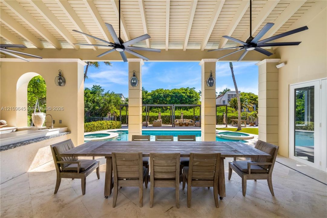 Covered patio featuring a beamed ceiling with dual overhead fans, stone flooring, a built-in outdoor kitchen, and pool with an integrated spa